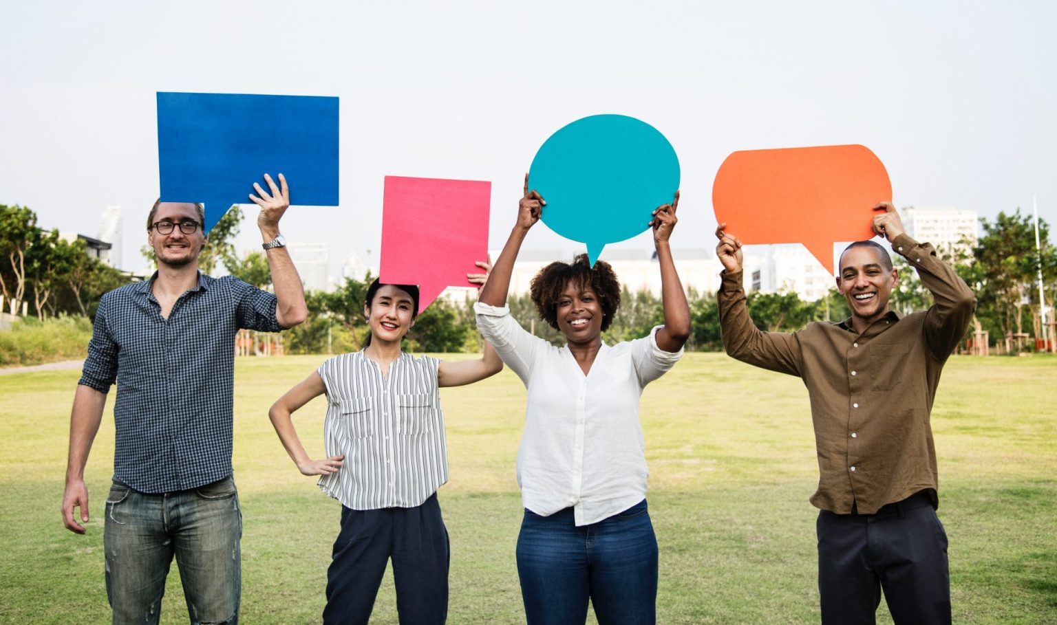 A group of people holding up colorful speech bubbles in a park, engaging in lively conversations.