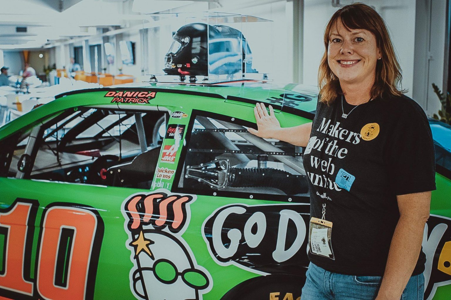 A woman standing next to a NASCAR car featuring the GoDaddy logo.
