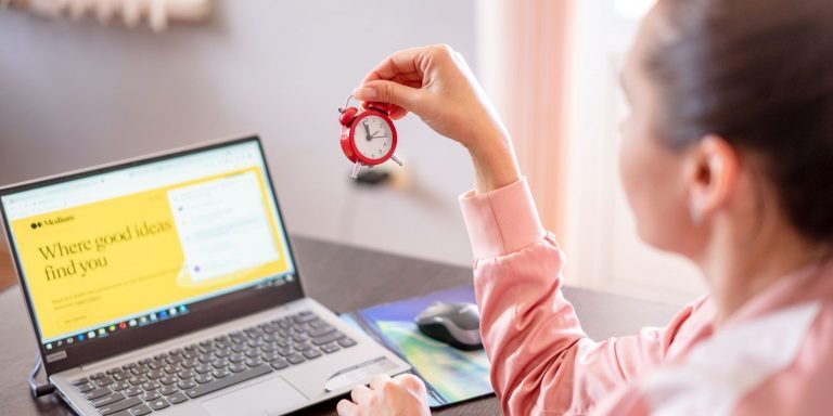 Woman holding a clock in front of a laptop